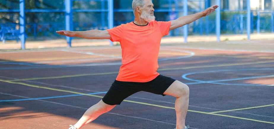 senior man in orange shirt and black pants doing yoga